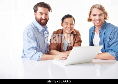 Tre prestanti giovani usando un computer portatile Foto Stock