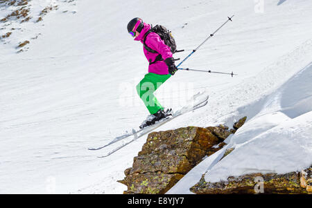 Sciatore salta fuori da una scogliera in montagna in una giornata di sole Foto Stock