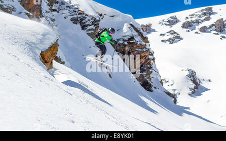 Donna sciatore salta fuori da una scogliera in montagna in una giornata di sole Foto Stock