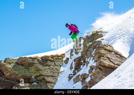 Sciatore salta fuori da una scogliera in montagna in una giornata di sole Foto Stock