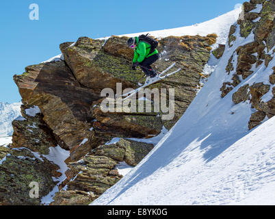 Donna sciatore salta fuori da una scogliera in montagna in una giornata di sole Foto Stock