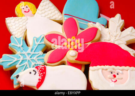 Close up splendidamente decorate iced biscotti di Natale su una targhetta rossa con soft, studio di illuminazione. Foto Stock