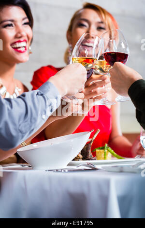 Amici asiatici, due coppie, a pranzo nel ristorante elegante mangiare bene e bere il vino Foto Stock