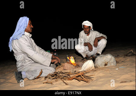 Due uomini beduino nel deserto intorno al campo di fuoco di notte sul deserto trek escursione, Sinai, Egitto Foto Stock