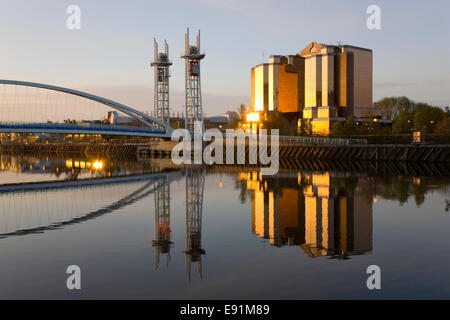 Salford Quays, Greater Manchester, Inghilterra. Il Quay West e il Millennium Bridge si riflette nel Manchester Ship Canal, sunrise. Foto Stock