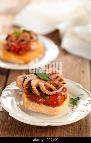 Il cibo italiano. Bruschetta con polipetti, pomodori e prezzemolo. Foto Stock