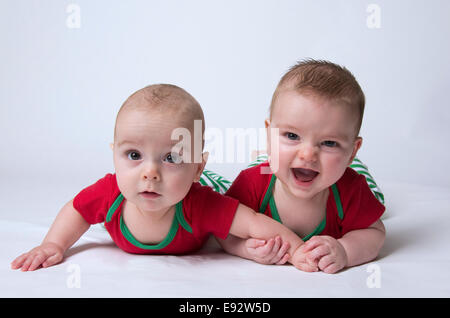 Molto felice di 9 mesi gemelli fraterni ragazzi indossando i colori di Natale, tenendo le mani e sorridente, durante la foratura fino le loro teste Foto Stock