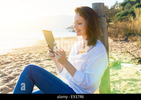 Donna che utilizza una tavoletta digitale sulla spiaggia Foto Stock