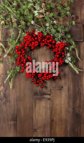Verde di Natale i rami degli alberi e corona da bacche rosse su legno rustico sfondo. festosa decorazione Foto Stock