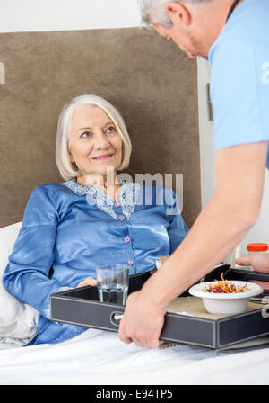 Custode che serve la prima colazione a felice donna senior Foto Stock