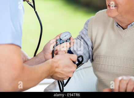 Medico maschio controllando la pressione del sangue di uomo senior Foto Stock