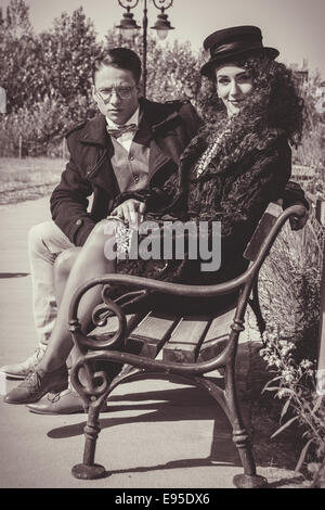 Moda giovane seduto sul banco in stile vintage e la donna che indossa cappotto e cappello per autunno Meteo Foto Stock