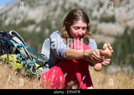 Donna strofinando il piedi su uno zaino viaggio in Oregon Wallowa della montagna. Foto Stock