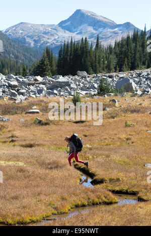 Donna attraversando un piccolo flusso su un viaggio zaino in Oregon Wallowa della montagna. Foto Stock