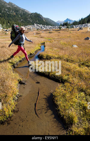 Donna attraversando un piccolo flusso su un viaggio zaino in Oregon Wallowa della montagna. Foto Stock
