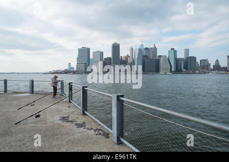 Uomo in pensione la pesca da un molo su Staten Island NY con una vista di Manhattan in background. Foto Stock
