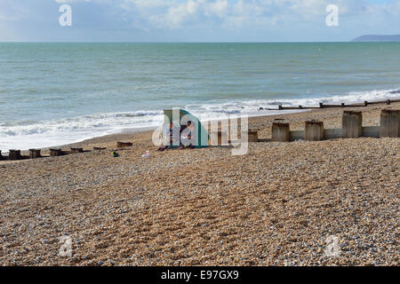 Una coppia matura si ripara dalla brezza del mare a Bexhill sulla spiaggia del mare. East Sussex Foto Stock