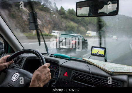 Accelerando le automobili veicoli in sorpasso su autostrada durante heavy rain shower visto dall'interno della vettura con GPS e road map sul cruscotto Foto Stock