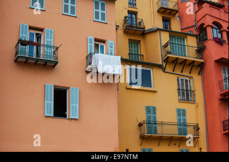 Balconi e finestre con tendine di color pastello delle case nella città di Menton lungo la Riviera Francese, Côte d'Azur, in Francia Foto Stock