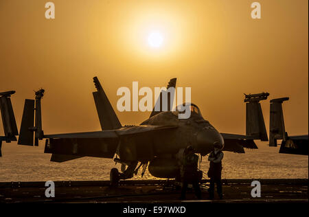 Un US Navy F/A-18E Super Hornet fighter aircraft si stagliano dal sole al tramonto sul ponte di volo della portaerei USS Carl Vinson durante le operazioni contro lo Stato islamico Ottobre 16, 2014 in mare Arabico. , Come la nave supporta inerenti a risolvere. Il presidente Barack Obama ha autorizzato gli aiuti umanitari le consegne in Iraq come pure le incursioni aeree mirate a proteggere il personale degli Stati Uniti dagli estremisti noto come lo stato islamico in Iraq e il levante. Stati Uniti Comando centrale diretto le operazioni. Foto Stock