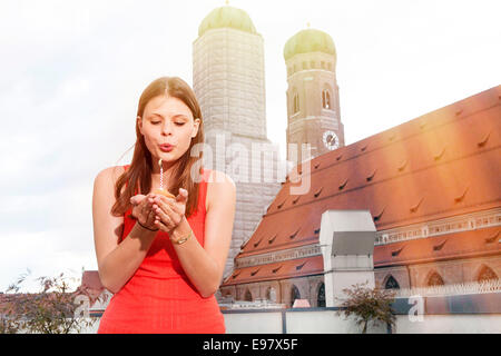 Giovane donna soffiando candela sulla terrazza sul tetto, Monaco di Baviera, Germania Foto Stock
