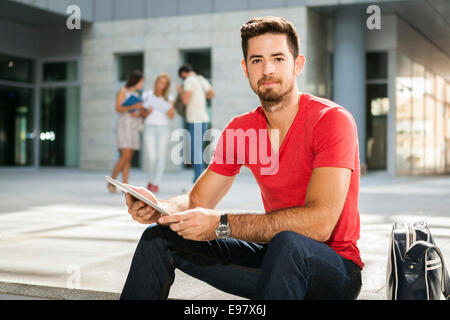 Studente maschio utilizzando digitale compressa, amici in background Foto Stock