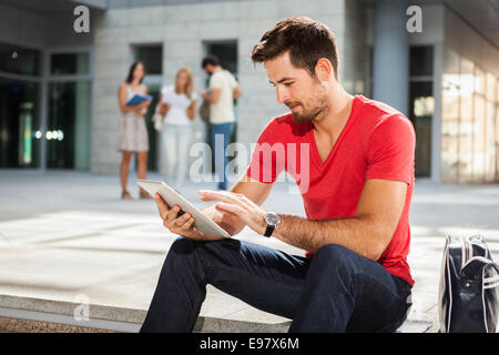 Studente maschio utilizzando digitale compressa, amici in background Foto Stock