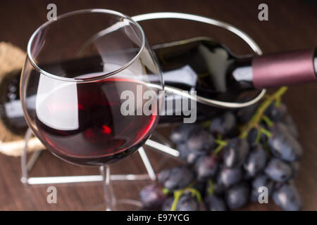 Wineglass con vino rosso con uve e bottiglia a sfondo Foto Stock