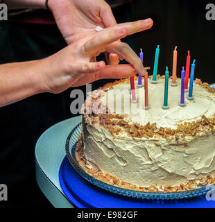 Contro lo sfondo nero due mani di illuminazione multicolore 9 candeline di compleanno sul toffee torta di compleanno matchstick. torta è su Foto Stock