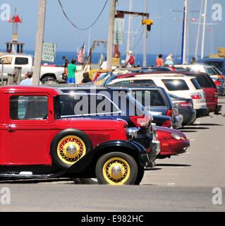 Un antico rosso luminoso giallo carrello ruote a razze parcheggiato di fronte linea moderna macchine parcheggiate su wharf in Rockport Massachusetts. Foto Stock
