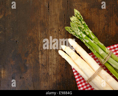 Freschi mazzi di verde e asparagi bianchi giacenti su un tovagliolo controllato su una trama della superficie in legno con copyspace Foto Stock