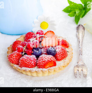 Piccolo servizio individuale di un fresco intero di fragola, ribes e mirtillo tart spolverato con zucchero su una dorata crosta croccante con una torta di argento forcella Foto Stock