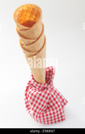 Angolo di alta vista di una pila di croccante vuoto coni di gelato con un punto rosso e bianco tovagliolo a scacchi Foto Stock