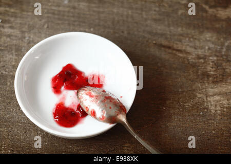 Argento cucchiaino appoggiato su un piccolo piatto bianco con campioni di fruttato confettura di fragole presi durante la preparazione di un lotto in cucina Foto Stock