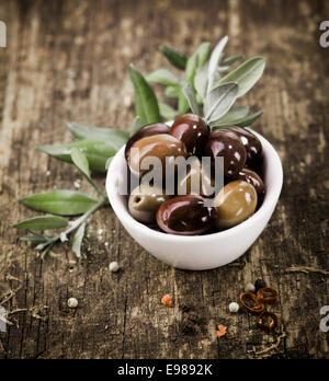 Ciotola riempita con appena raccolto intero fresco di olive nere su un rustico tavolo in legno Foto Stock