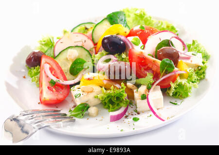 Una sana insalata greca per il pranzo con nitide foglie verdi, olive, feta, cipolla, pomodoro, cetriolo e ravanelli su sfondo bianco Foto Stock