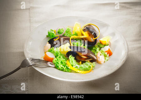 Servire su un piatto di cozze fresche e insalata di mare con foglie verdi, granchi e gamberi guarnita con buccia di arancia Foto Stock