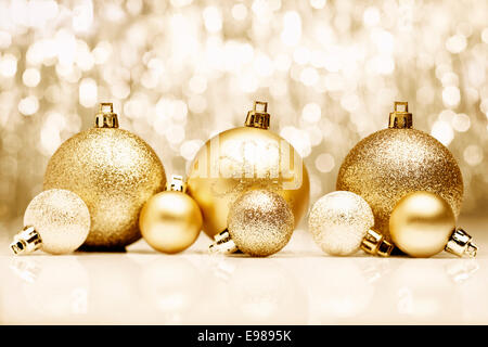 Una disposizione di golden baubles di Natale contro un festoso bokeh di oro scintillanti luci con copyspace Foto Stock