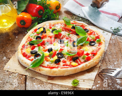 Deliziosa pizza fatta in casa con una spessa base oro sormontato con formaggio, pomodori, peperoni, olive ed erbe Foto Stock