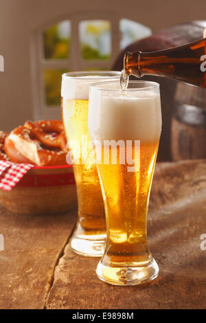 Versando bicchieri di Spumeggiante birra dorata in bicchieri alti da una bottiglia di vetro marrone in un pub o ristorante Foto Stock