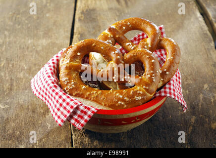 Croccante di color oro-marrone pretzel rivestito in semi in una ciotola con un controllato colorati in rosso e bianco igienico su una tavola in legno rustico Foto Stock