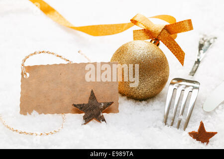 Luogo di festa impostazione con decorazioni di Natale e le posate d'argento in neve fresca con una decorazione blank gift tag Foto Stock