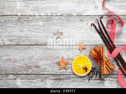 Array colorato decorativo di spezie di Natale con un rosso fresco e bianco a scacchi twirled nastro su uno sfondo di grungy textured weathered legno bianco Foto Stock