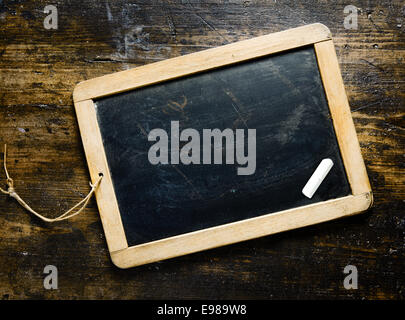 Smal incorniciate di legno lavagna vuota con un pezzo di chalk su un legname darl sfondo con grana di legno adatto per il messaggio di saluto, messaggio o menu Foto Stock