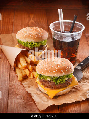 Due hamburger e patatine fritte su carta marrone con bicchiere di bibite Foto Stock