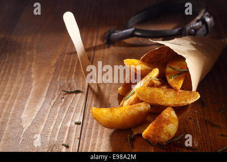 Deliziosi snack di spezie golden Spicchi di patate che sono stati fritti o al forno la fuoriuscita di un marrone rotolo di carta su un tavolo di legno Foto Stock