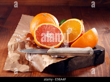 Succose arance, uno insieme e alcuni tagliate a metà su carta marrone con coltello Foto Stock