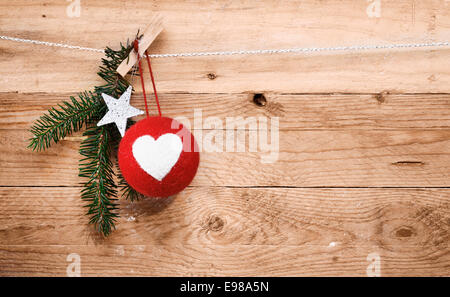 Paese natale decorazioni con un rosso tessuto artigianale ninnolo decorato con un cuore e una stella e rametto di pino appeso su una linea superiore naturali di tavole di legno con grana di legno e texture copyspace Foto Stock