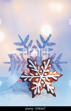 Iced decorativo gingerbread Natale biscotto di fiocco di neve con un ornamento fiocco di neve contro un morbido bokeh di fondo della parte luci con copyspace Foto Stock