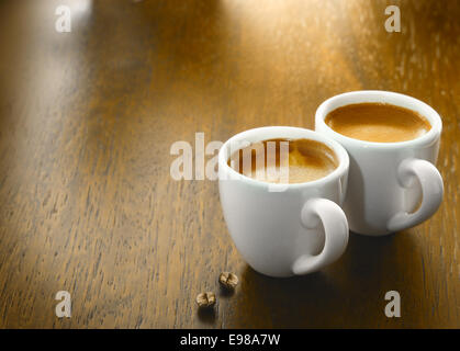 Due tazze di caffè appena macinato il caffè con due singoli chicchi di caffè su una superficie strutturata tavolo in legno top con copyspace Foto Stock